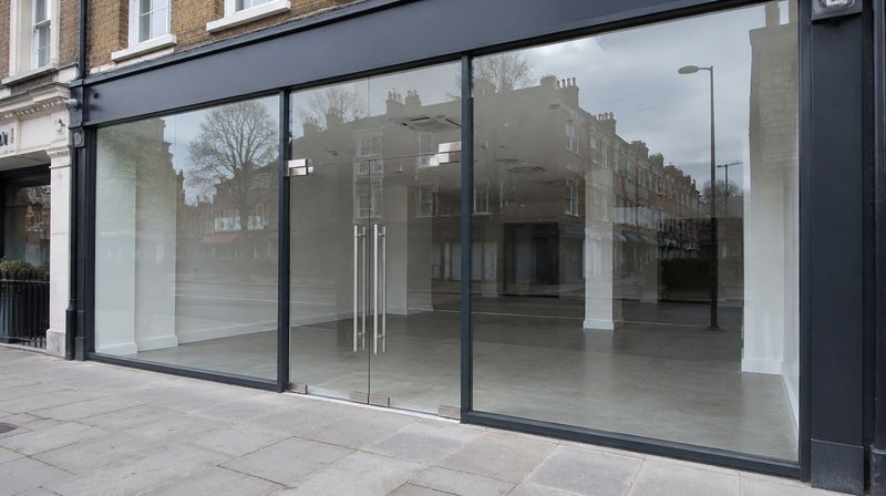 A shopfront glazed with large toughened panes in slim frames and a glass entrance door on patch fittings